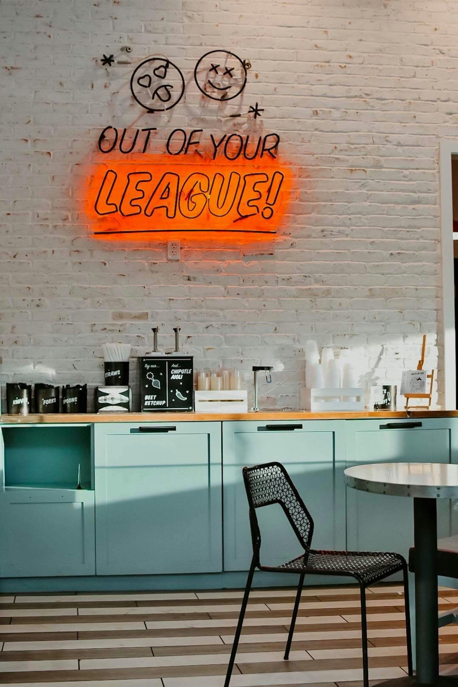 Stylish dining area featuring contemporary furniture and a vibrant neon sign saying 'Out of Your League.'